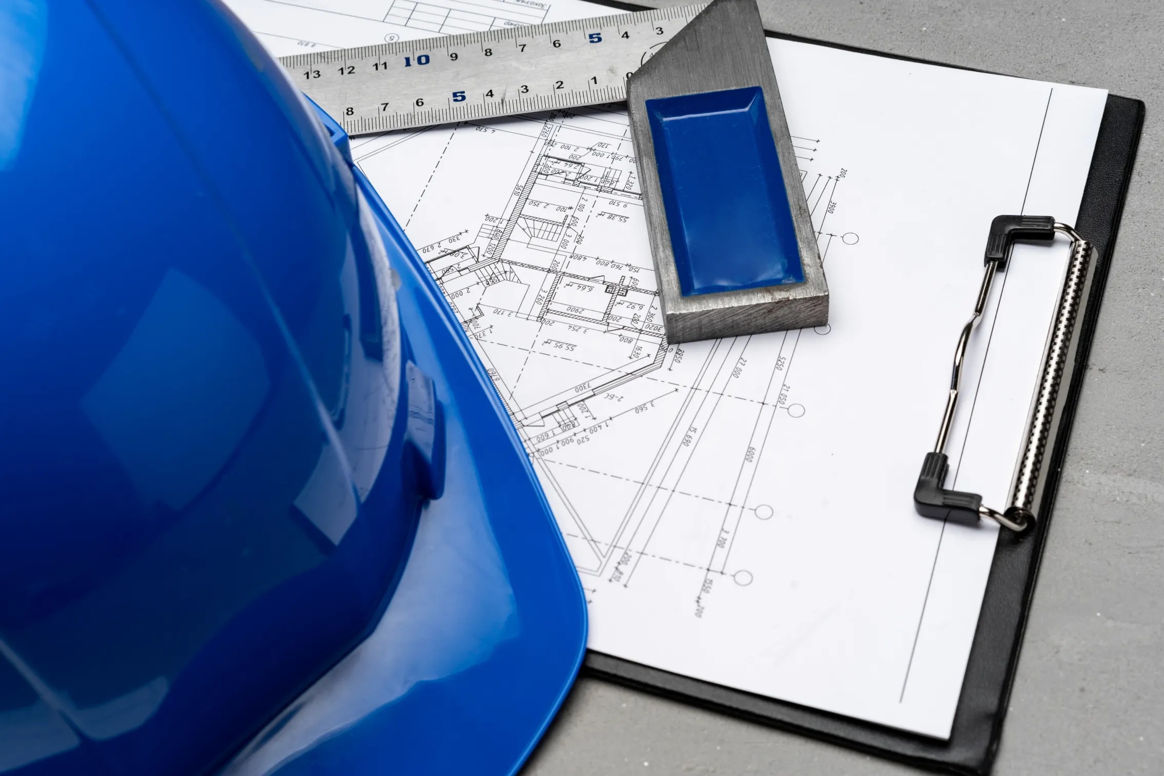 blue hard hat beside blueprints and clipboard on desk